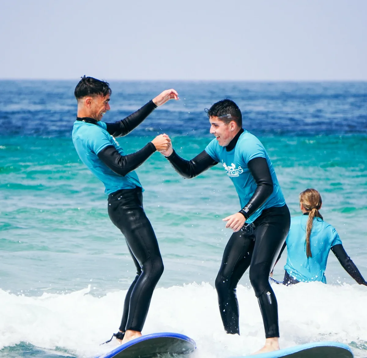 Two students high-fiving on their surfboards after a successful lesson